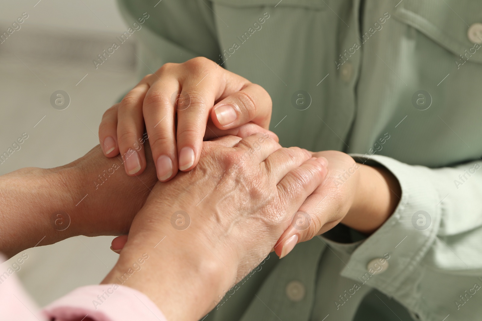 Photo of Young and elderly women holding hands indoors, closeup