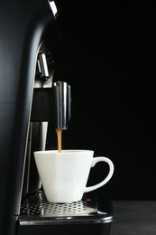 Photo of Modern espresso machine pouring coffee into cup on grey table against black background