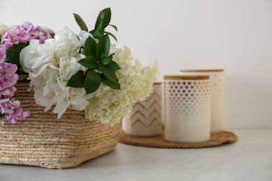 Beautiful hydrangea flowers in basket and jars on light table, closeup