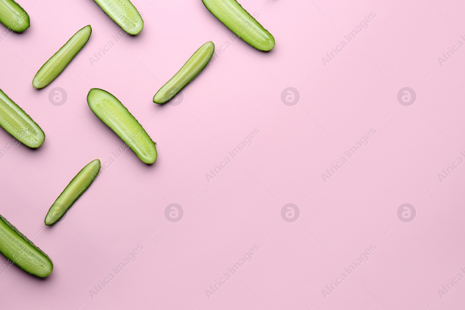 Photo of Cut fresh ripe cucumbers on light pink background, flat lay. Space for text