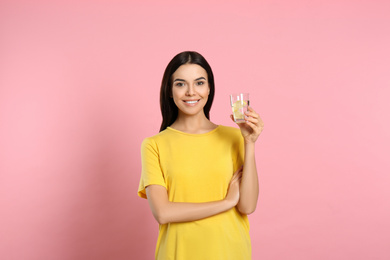 Beautiful young woman with tasty lemon water on pink background