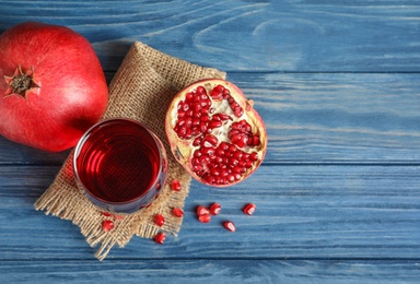 Photo of Glass of pomegranate juice and fresh fruits on wooden background, top view with space for text