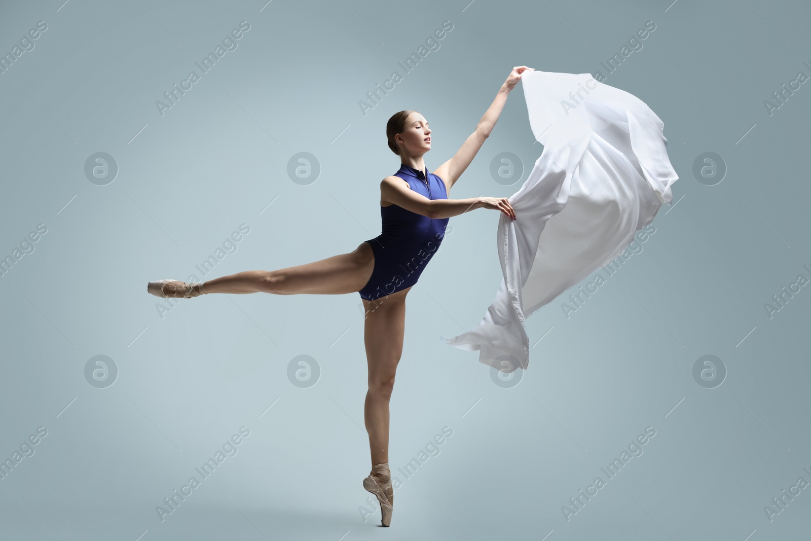 Photo of Graceful young ballerina practicing dance moves with veil on grey background