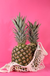 Whole ripe pineapples and net bag on pink background