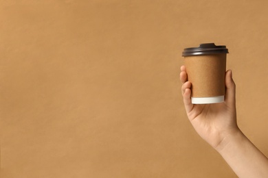Photo of Woman holding takeaway paper coffee cup on brown background, closeup. Space for text