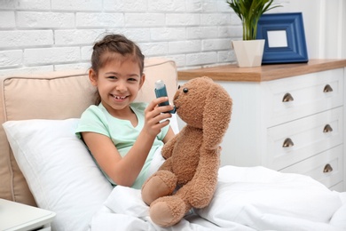 Photo of Cute child playing doctor with stuffed toy on bed in hospital ward