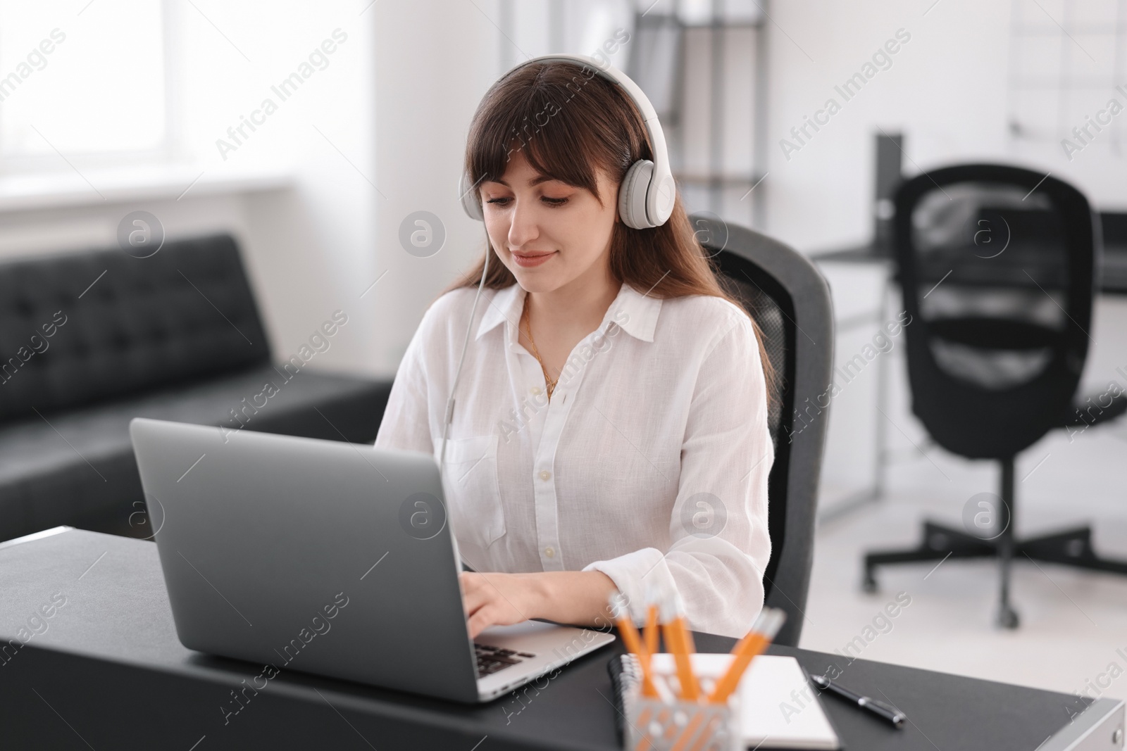 Photo of Woman in headphones watching webinar at table in office