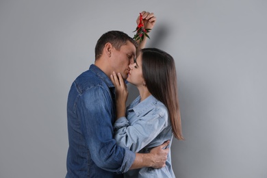 Photo of Happy couple kissing under mistletoe bunch on grey background