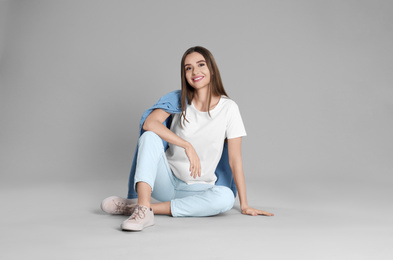 Photo of Young woman in stylish jeans sitting on grey background