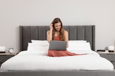 Happy woman with laptop on bed in bedroom