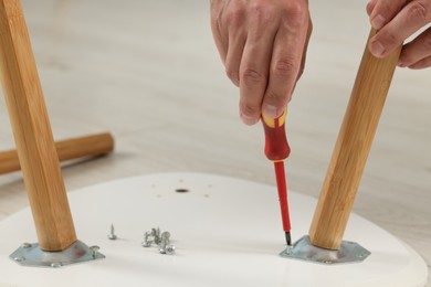 Photo of Man with screwdriver assembling furniture on floor, closeup