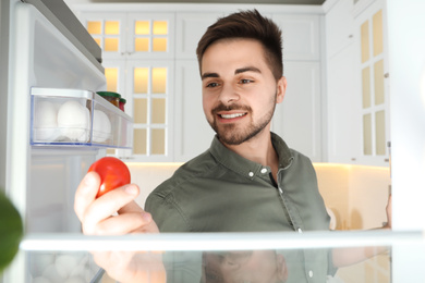 Photo of Young man looking into refrigerator, view from inside