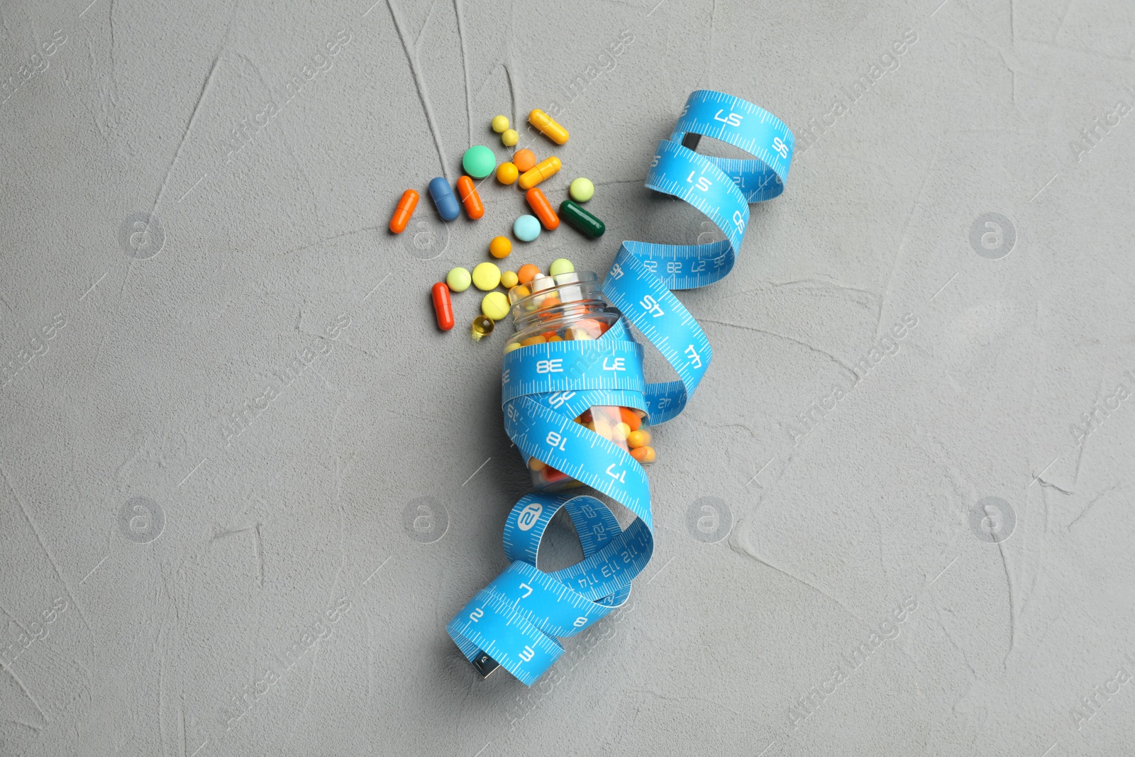 Photo of Jar of weight loss pills and measuring tape on grey table, flat lay