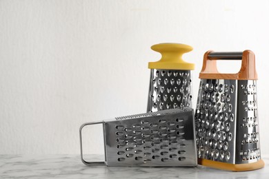 Photo of Different modern graters on white marble table. Space for text