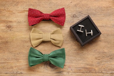 Photo of Stylish color bow ties and box of cufflinks on wooden background, flat lay