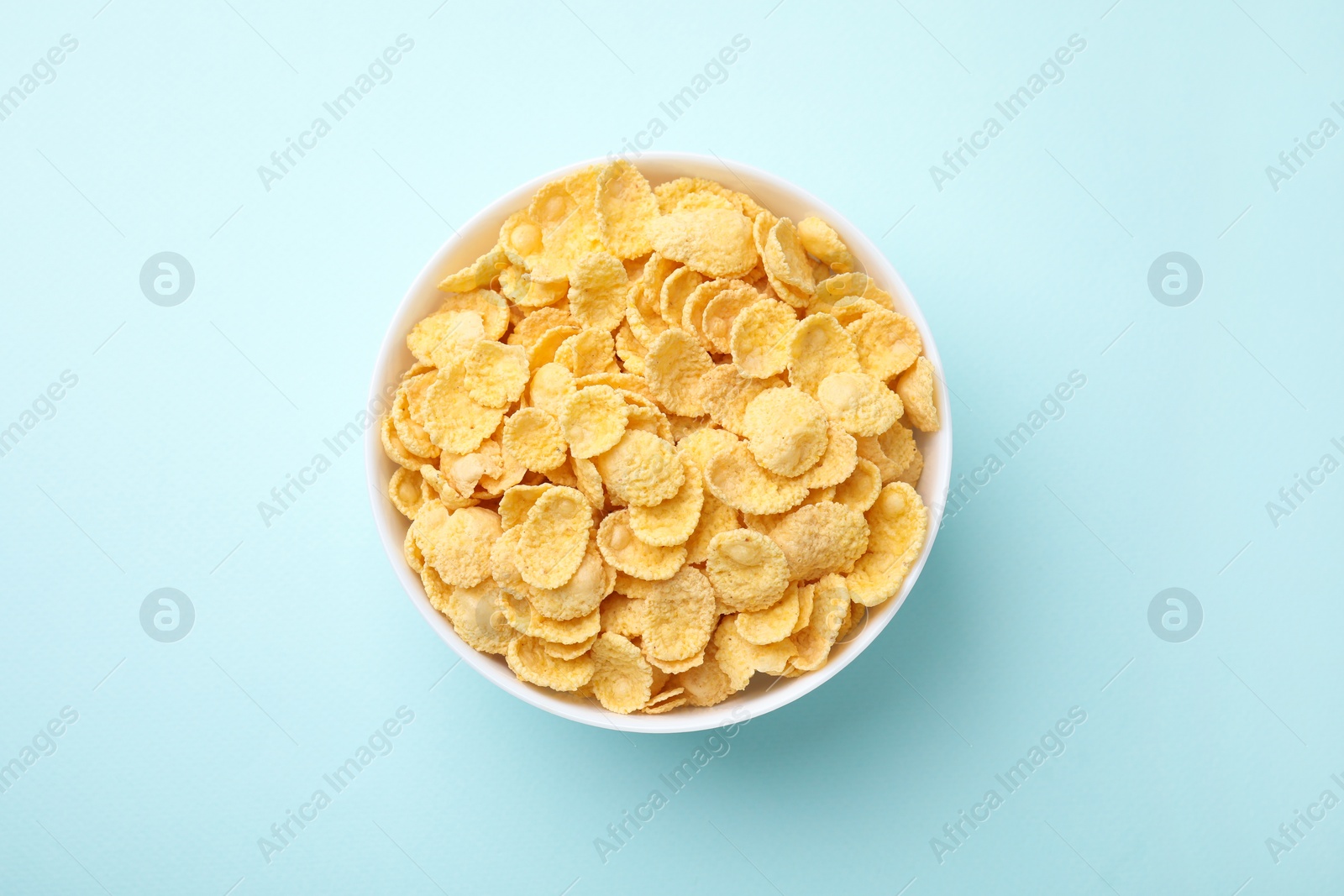 Photo of Breakfast cereal. Tasty corn flakes in bowl on light blue table, top view