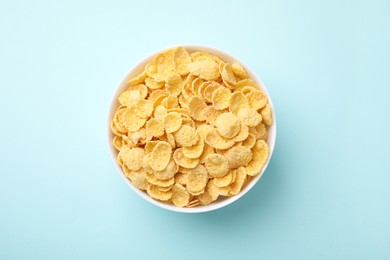 Photo of Breakfast cereal. Tasty corn flakes in bowl on light blue table, top view