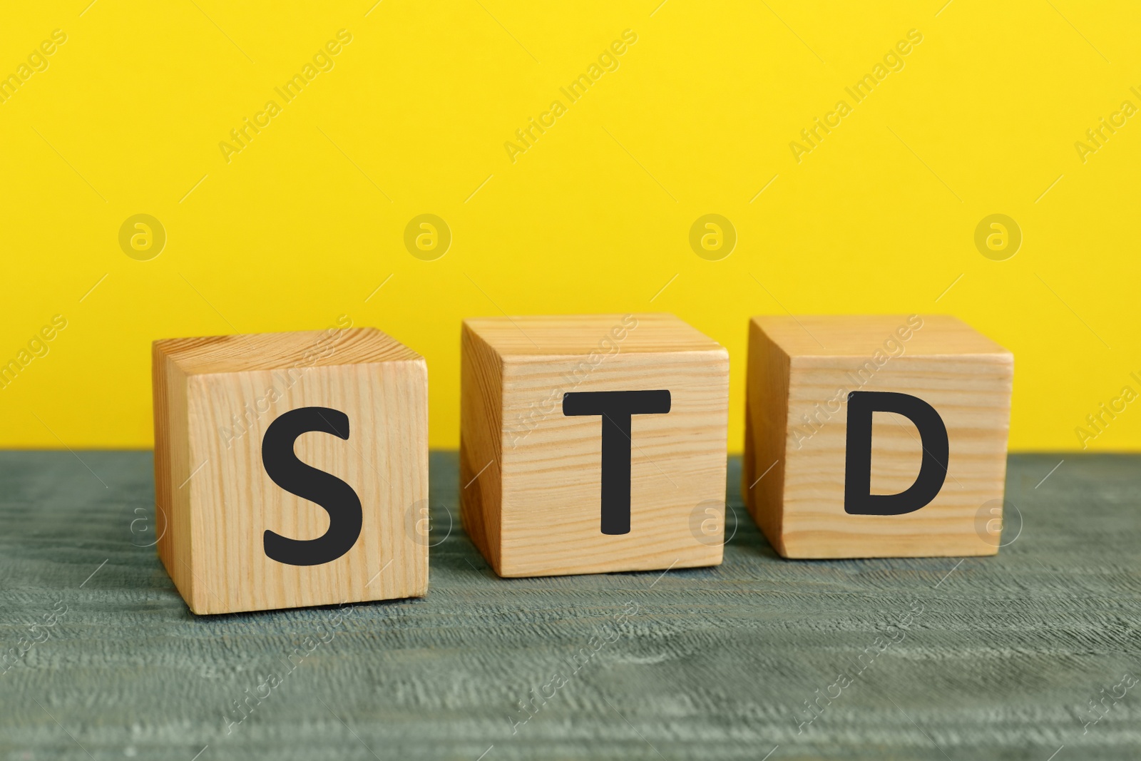 Photo of Abbreviation STD made with cubes on wooden table against yellow background