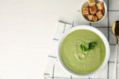 Delicious broccoli cream soup served on white wooden table, flat lay. Space for text