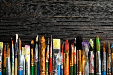 Photo of Different paint brushes on wooden background, top view with space for text