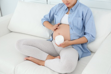 Photo of Pregnant woman applying body cream on belly at home, closeup