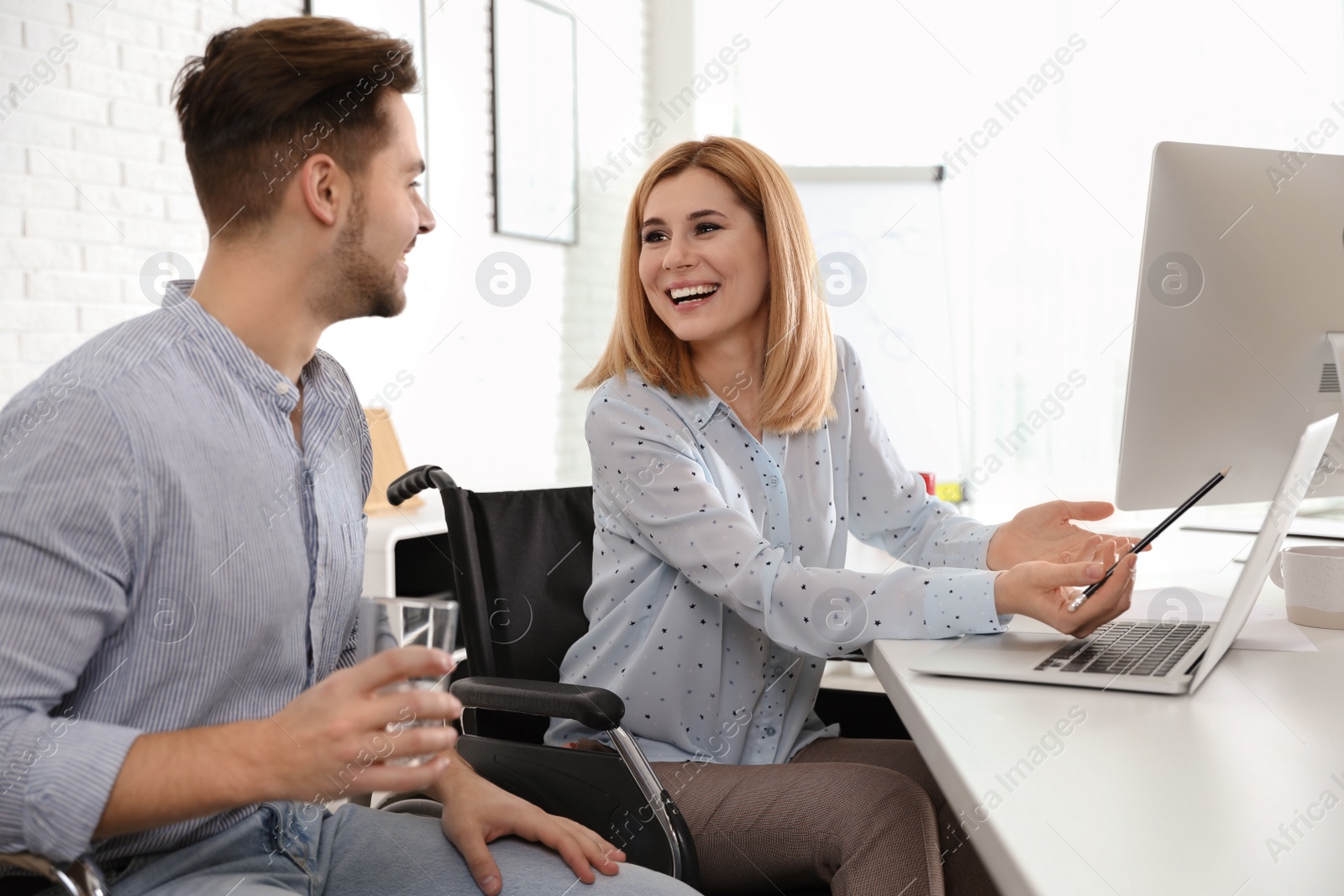 Photo of Woman in wheelchair with her colleague at workplace