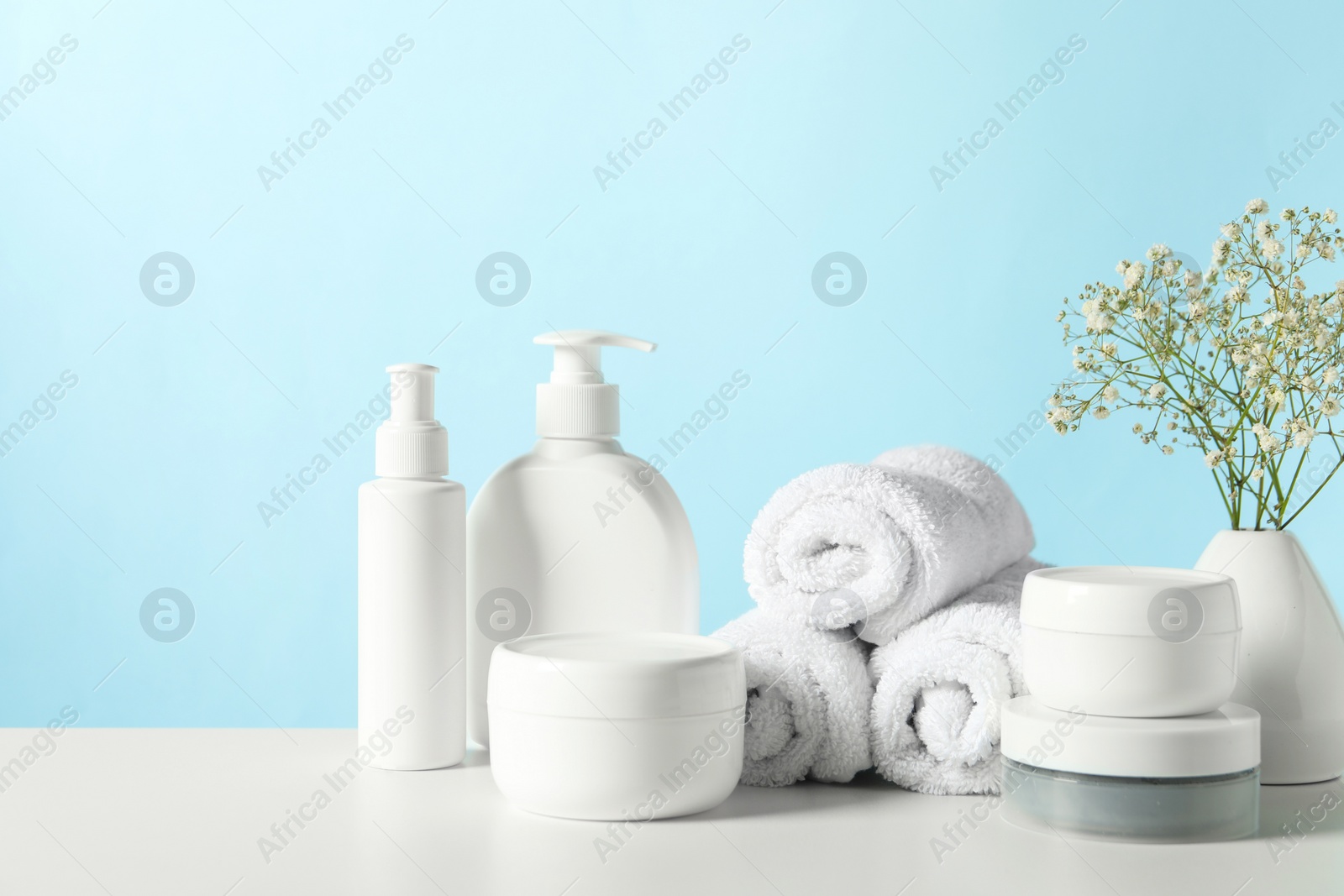 Photo of Different bath accessories and gypsophila on white table against light blue background