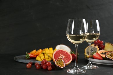 Photo of Delicious exotic fruits and glasses of wine on black table, space for text
