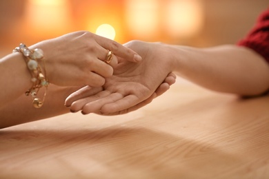 Chiromancer reading lines on woman's palm at table, closeup