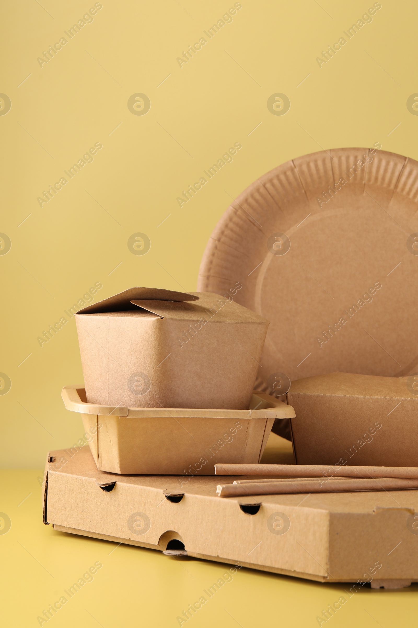 Photo of Eco friendly food packaging. Paper containers and tableware on pale yellow background