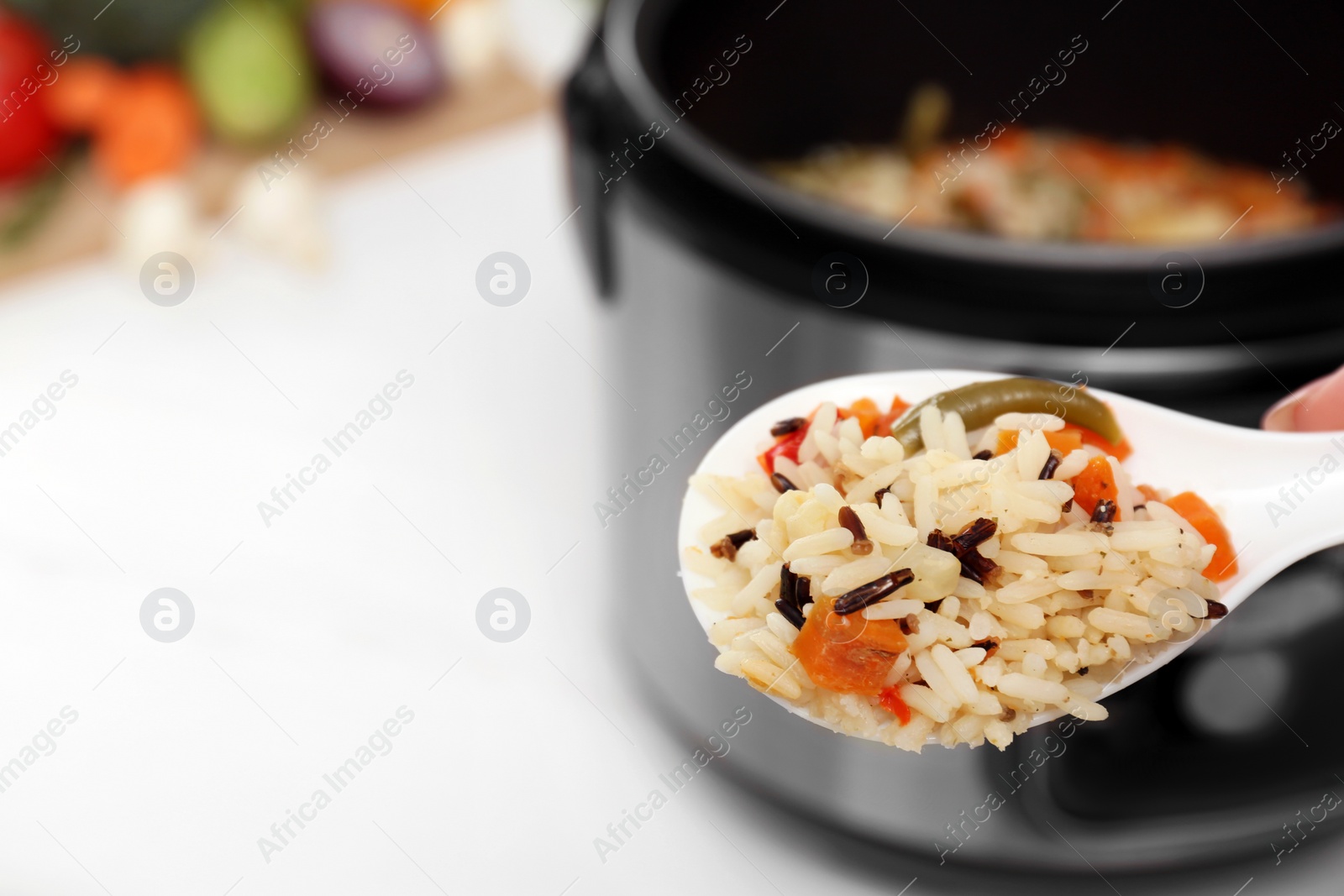 Photo of Spoon of rice with vegetables on blurred background, space for text. Multi cooker recipe