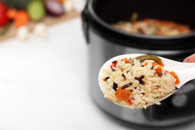 Spoon of rice with vegetables on blurred background, space for text. Multi cooker recipe