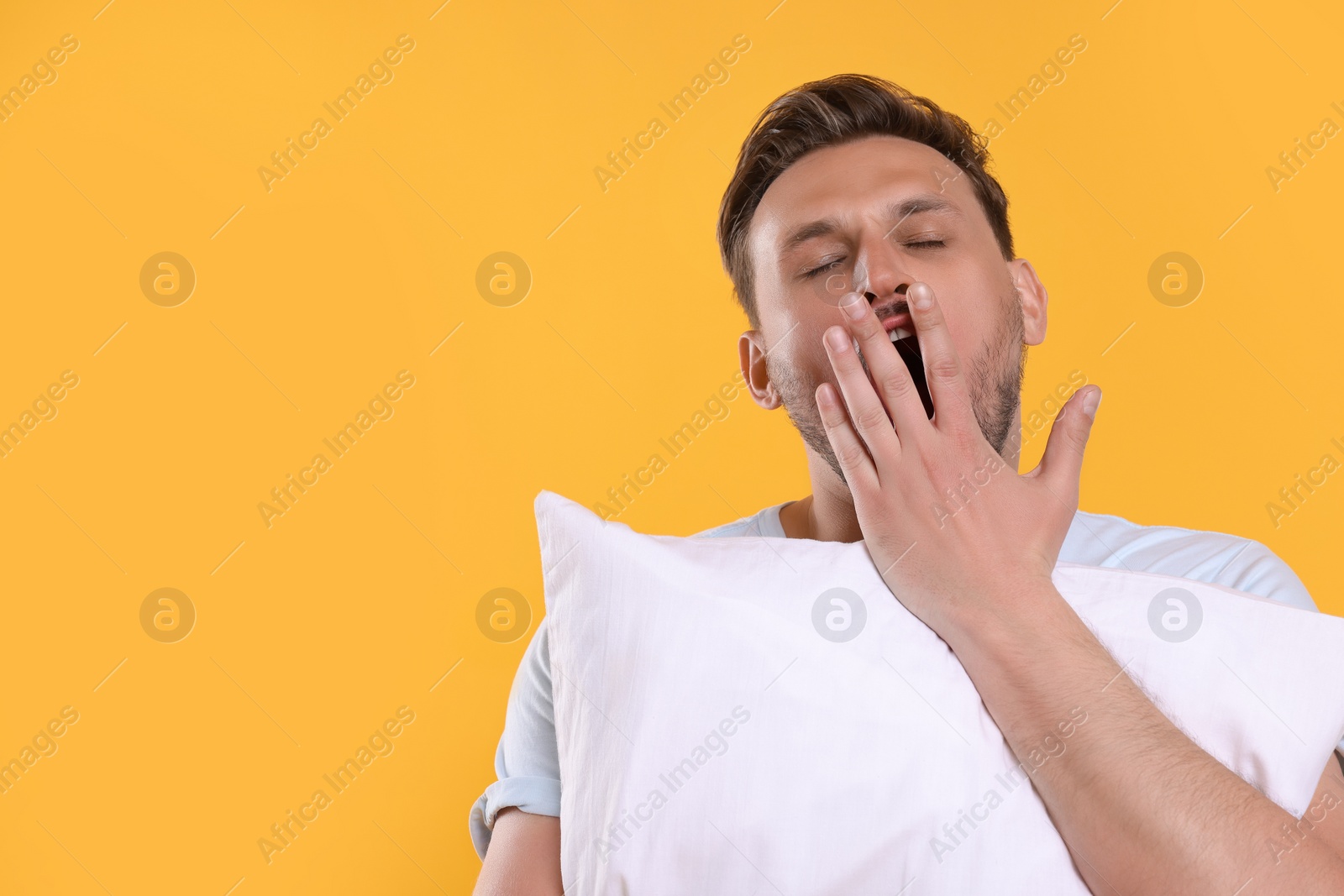 Photo of Sleepy man with pillow yawning on yellow background, space for text. Insomnia problem
