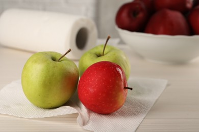 Photo of Fresh apples and paper towel on light wooden table, closeup