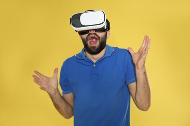 Emotional young man playing video games with virtual reality headset on color background