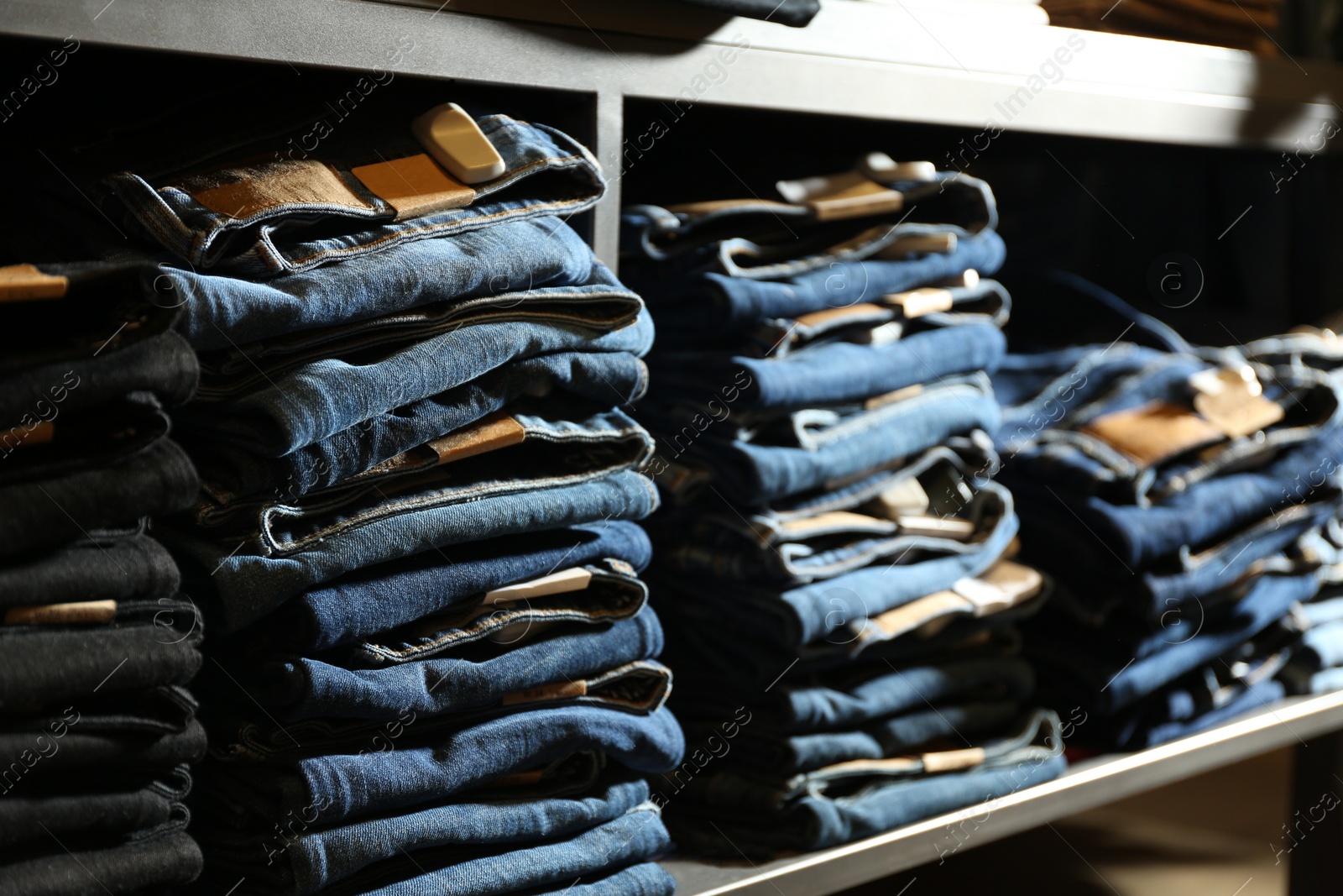 Photo of Collection of stylish jeans on shelf in shop