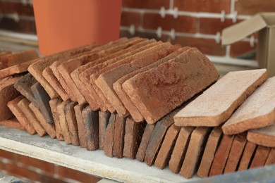 Photo of Many decorative bricks on scaffolding near wall, closeup. Tiles installation process
