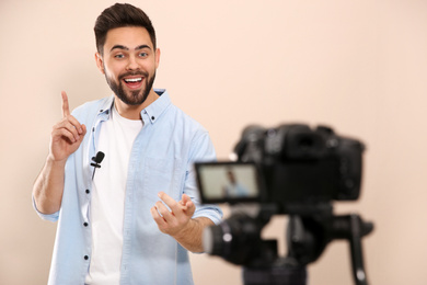 Photo of Young blogger recording video on camera against beige background