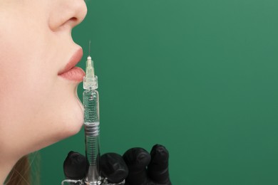 Cosmetologist with syringe on green background, closeup. Space for text