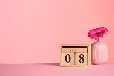 Photo of Calendar and vase with flower on table against color background, space for text. International Women's Day