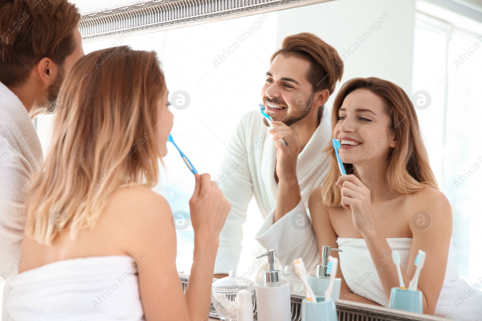 Photo of Young couple with toothbrushes near mirror in bathroom. Personal hygiene