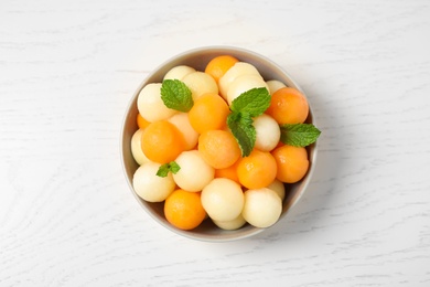 Photo of Melon balls and mint in bowl on white wooden table, top view