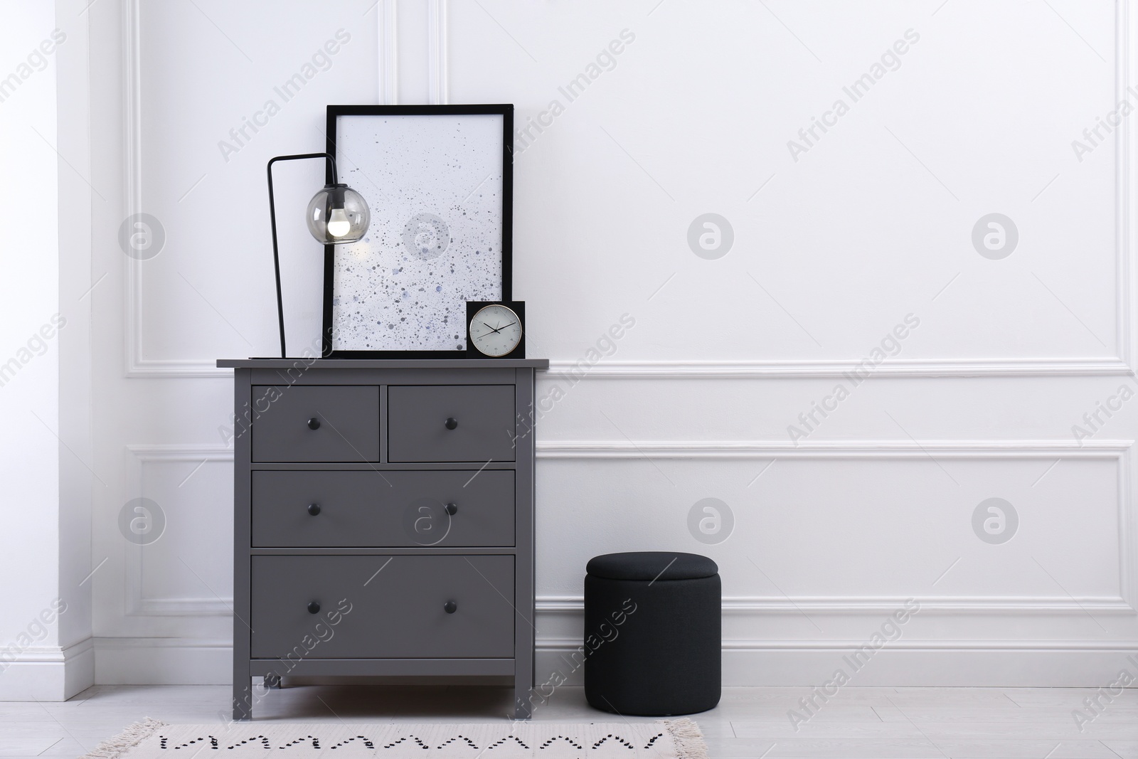 Photo of Grey wooden chest of drawers with lamp, clock and picture near white wall in room, space for text. Interior design