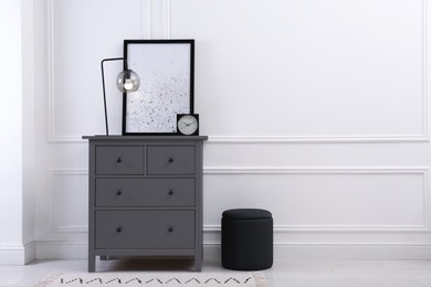 Photo of Grey wooden chest of drawers with lamp, clock and picture near white wall in room, space for text. Interior design