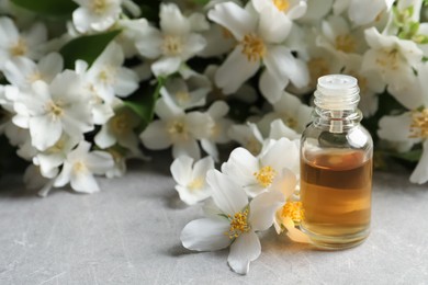 Photo of Jasmine essential oil and fresh flowers on light grey table, space for text