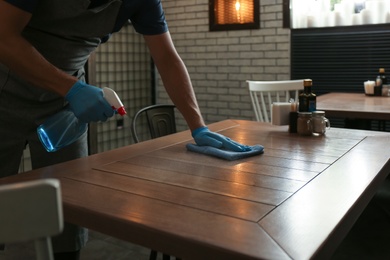 Photo of Waiter in gloves disinfecting table at cafe, closeup