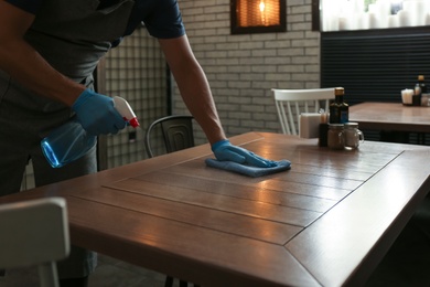 Waiter in gloves disinfecting table at cafe, closeup