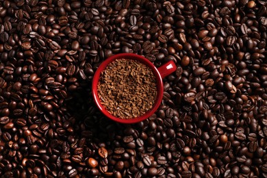 Photo of Cup with instant coffee on roasted beans, top view