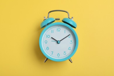 Photo of Alarm clock on yellow background, top view. School time