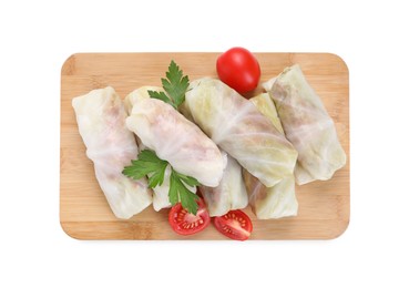 Photo of Wooden board with raw cabbage rolls, tomatoes and parsley isolated on white, top view